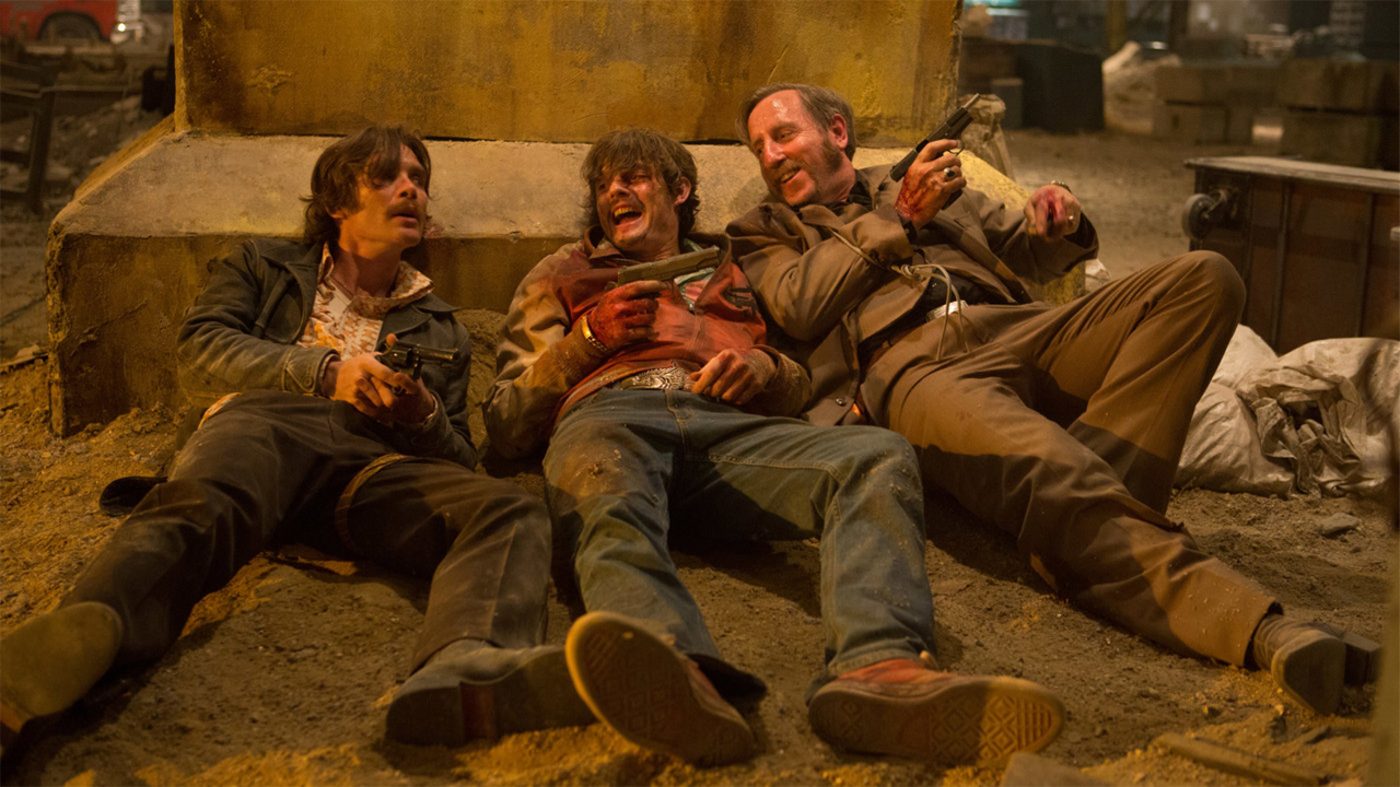 Drei Männer mit Pistolen liegen lachend am Boden