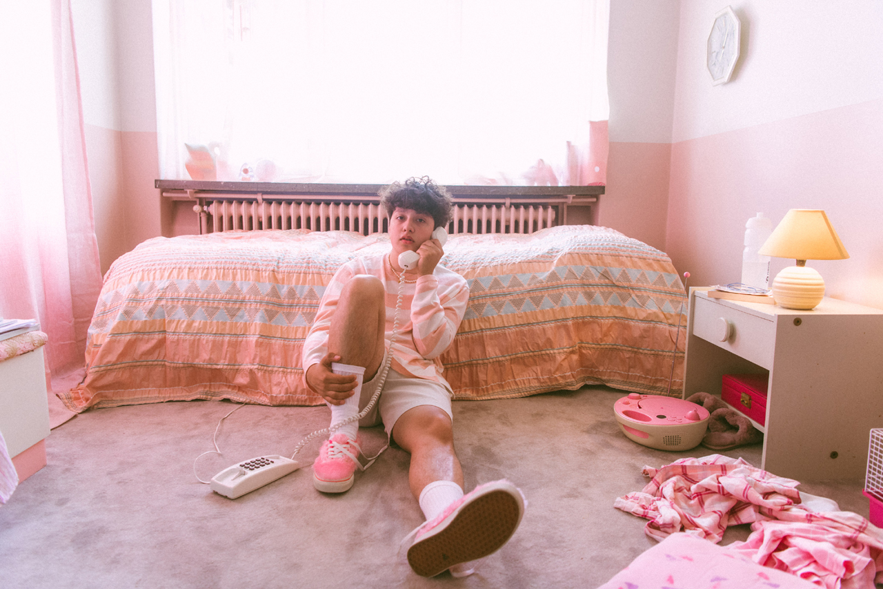 Boy Pablo sitzt in einem rosaroten Schlafzimmer auf dem Boden und telefoniert