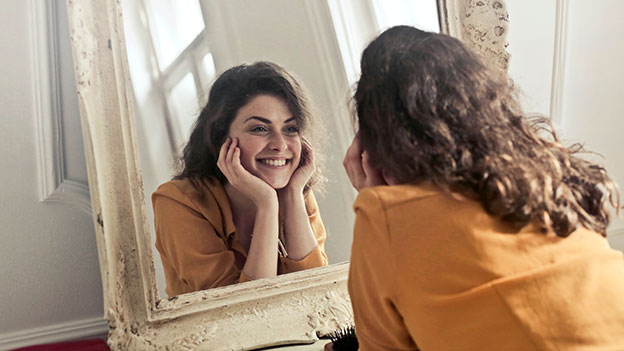 Frau lacht in einen Spiegel