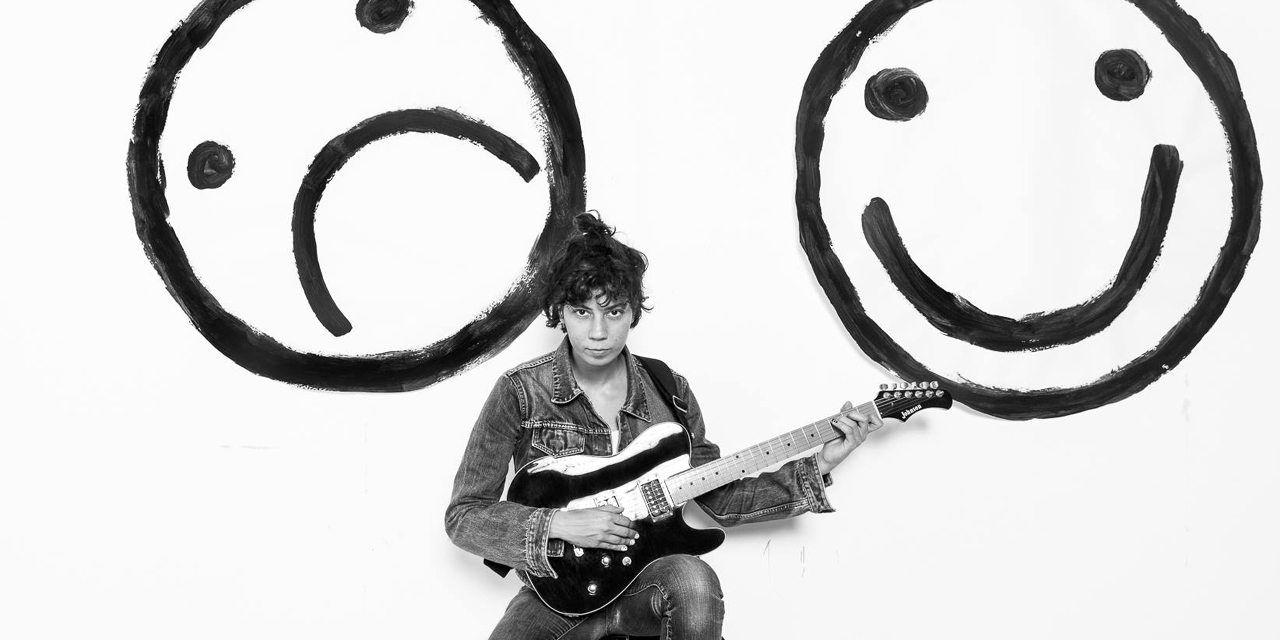 Monsterheart mit Gitarre sitzt vor zwei Smileys: eines lacht, eines weint