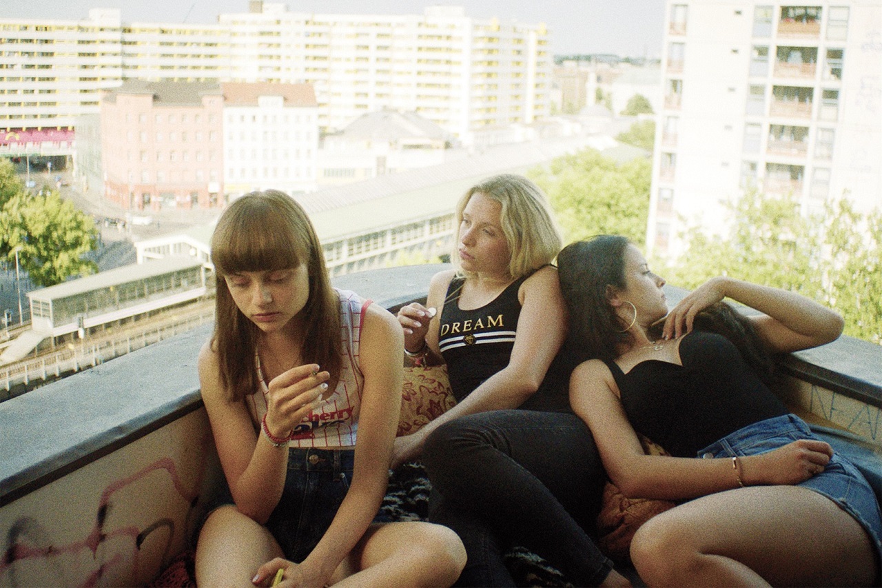 Drei Teenager sitzen auf einem Balkon auf einem Siedlungshaus am Kottbusser Tor in Berlin. Filmstill aus "Kokon".