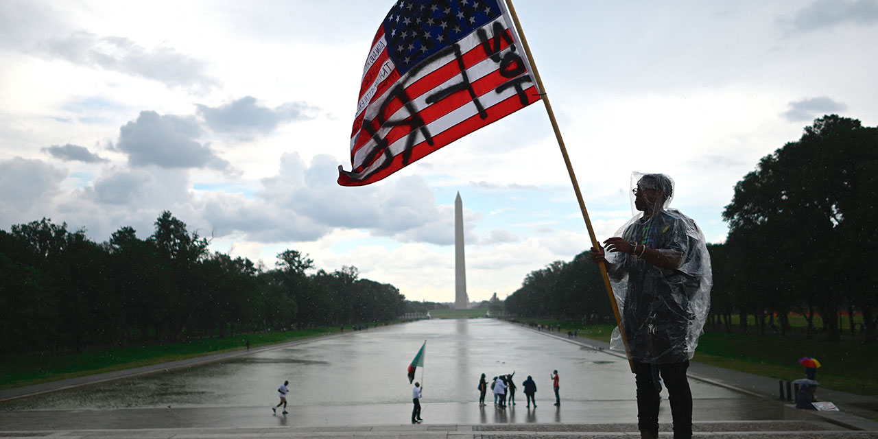 A demonstrator waves an American flag with the words "Not Free" painted on it in front of the Washington Monument during a Juneteenth march and rally in Washington, DC, on June 19, 2020.
