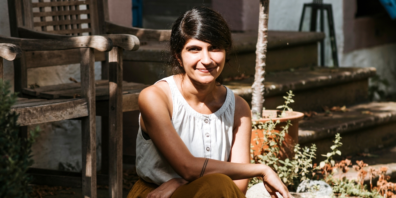 Autorin Shida Bazyar mit weißem, ärmellosem Top sitzt auf Stufen in einem Garten