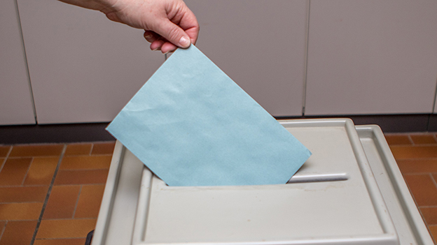 Ein Stimmzettel wird in eine Wahlurne geworfen