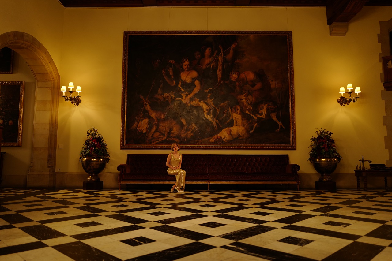Kristen Stewart sitzt allein auf einer Bank im Gang eines Palasts. Eine Szene aus "Spencer".