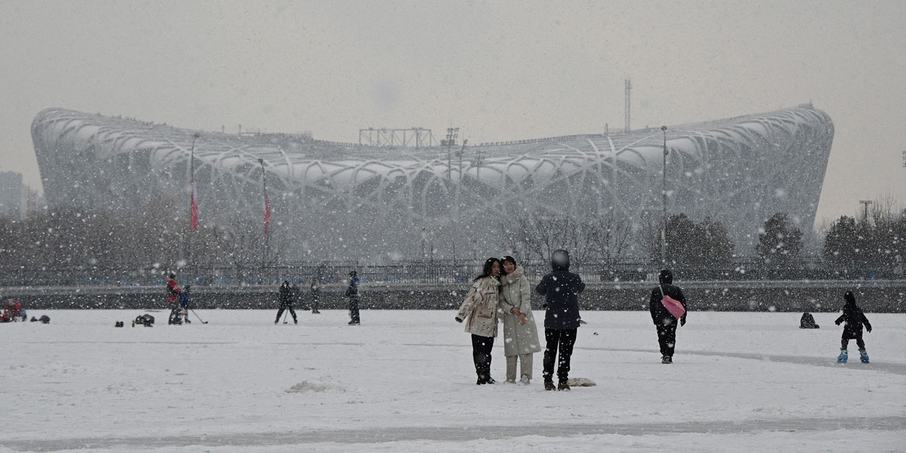 Menschen fotografieren sich vor dem Olympiastadion in Peking. Es schneit.