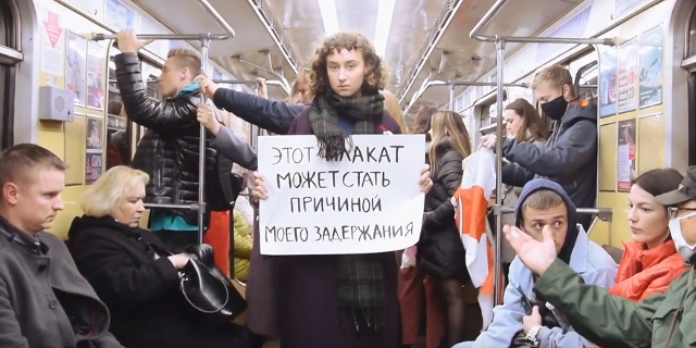 Eine junge Frau steht in einer U-Bahn mit einem Plakat in der Hand
