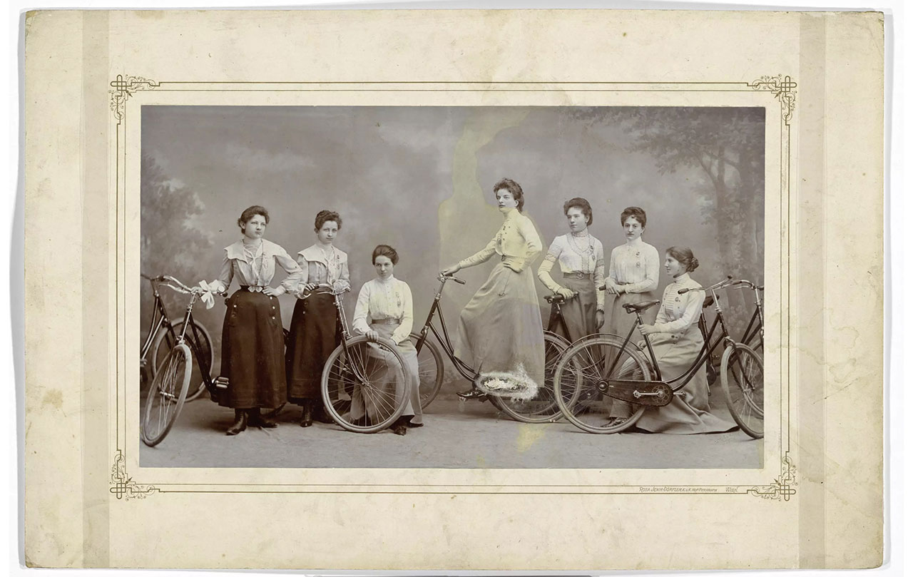 Gruppenporträt von sieben Frauen mit Fahrrädern, aufgenommen im Atelier. Die Frauen dürften Mitglieder eines Fahrradvereins/Bicycle Clubs gewesen sein