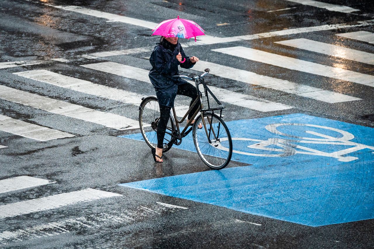 A morning commuter on her bicycle clutches an umbrella waiting at a red light is caught in a downpour, in the Danish capital Copenhagen on June 19, 2020.