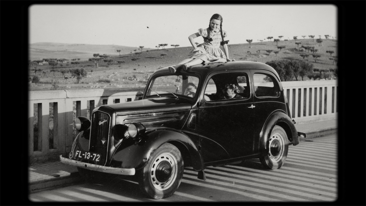 Ein altes Foto zeigt ein Mädchen auf einem Auto in Portugal Ende der 1940er Jahre. Filmstill aus "Journey to the sun".