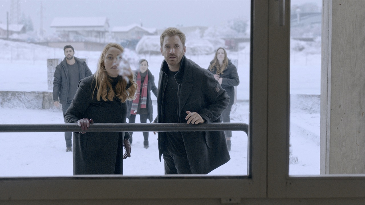 Junge Erwachsene schauen durch eine Glasfront im Winter, es liegt Schnee. Szene aus "After the Winter".