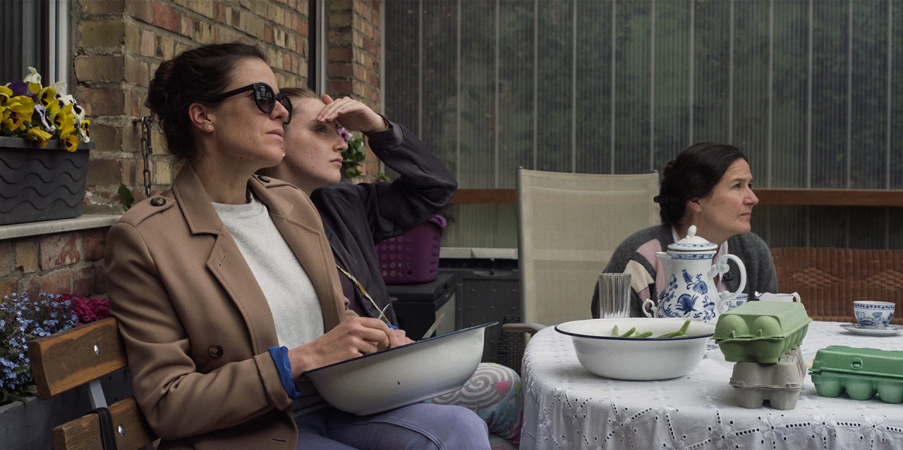 Szene aus dem Spielfilm "Alle reden übers Wetter": Drei Menschen sitzen auf einer Bank an einem Tisch im Freien.
