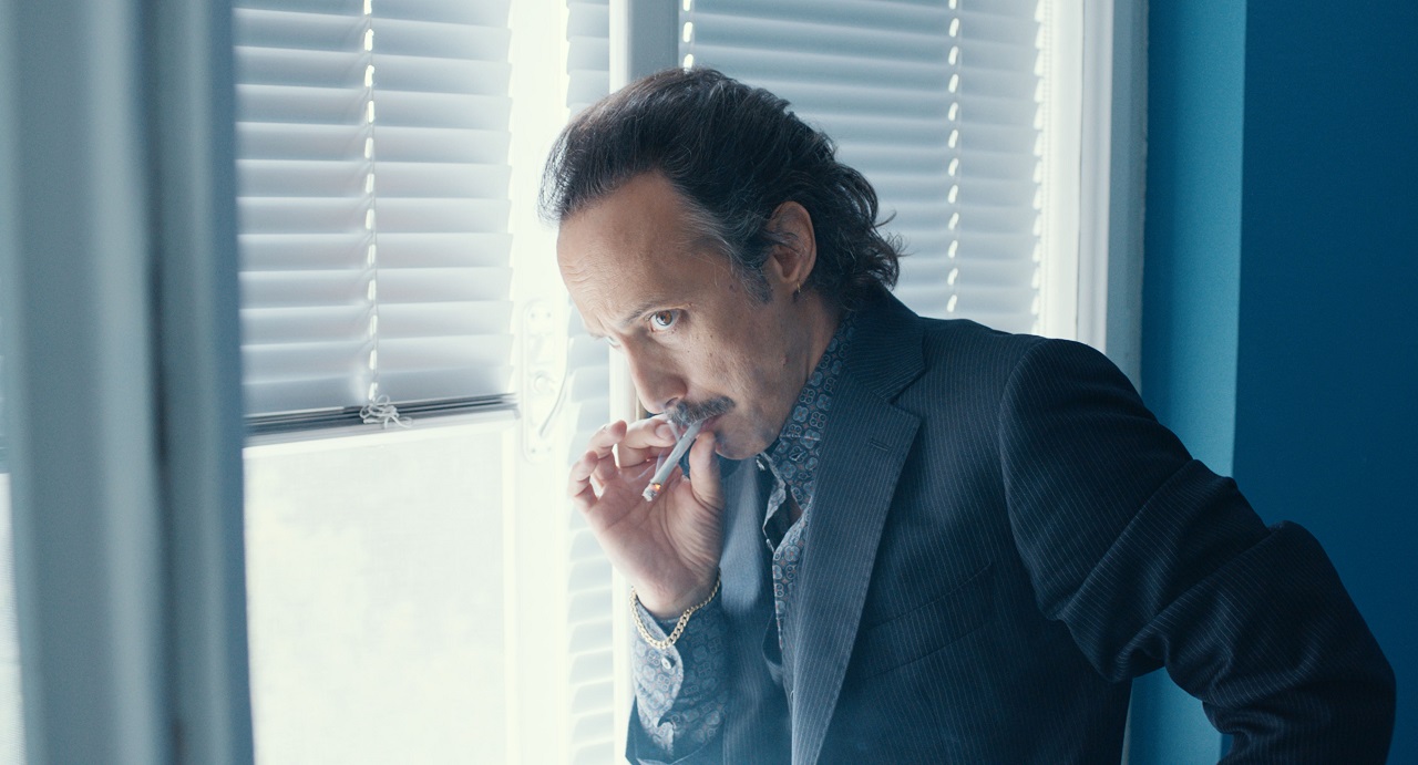 Michael Ostrowski raucht eine Zigarette neben enem Fenster, Szene aus "The Hawk/Der Onkel".