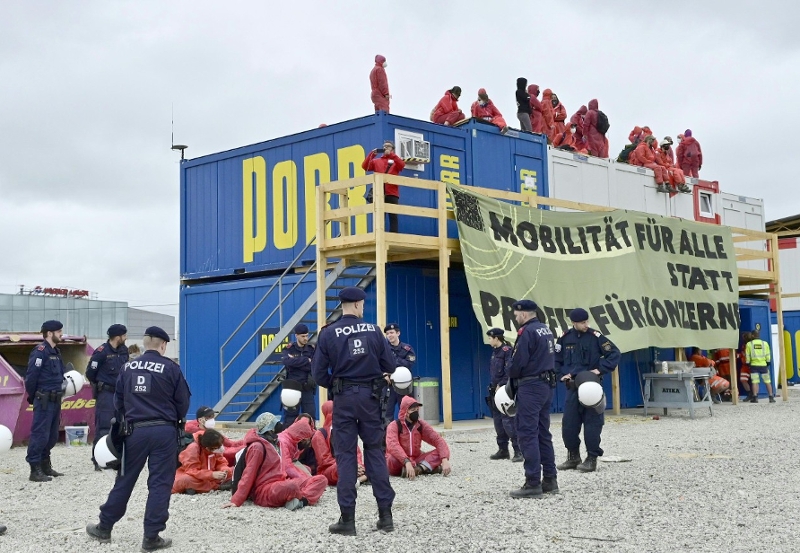 Aktivistinnen sitzen auf Baucontainer und vor Polizei am Boden