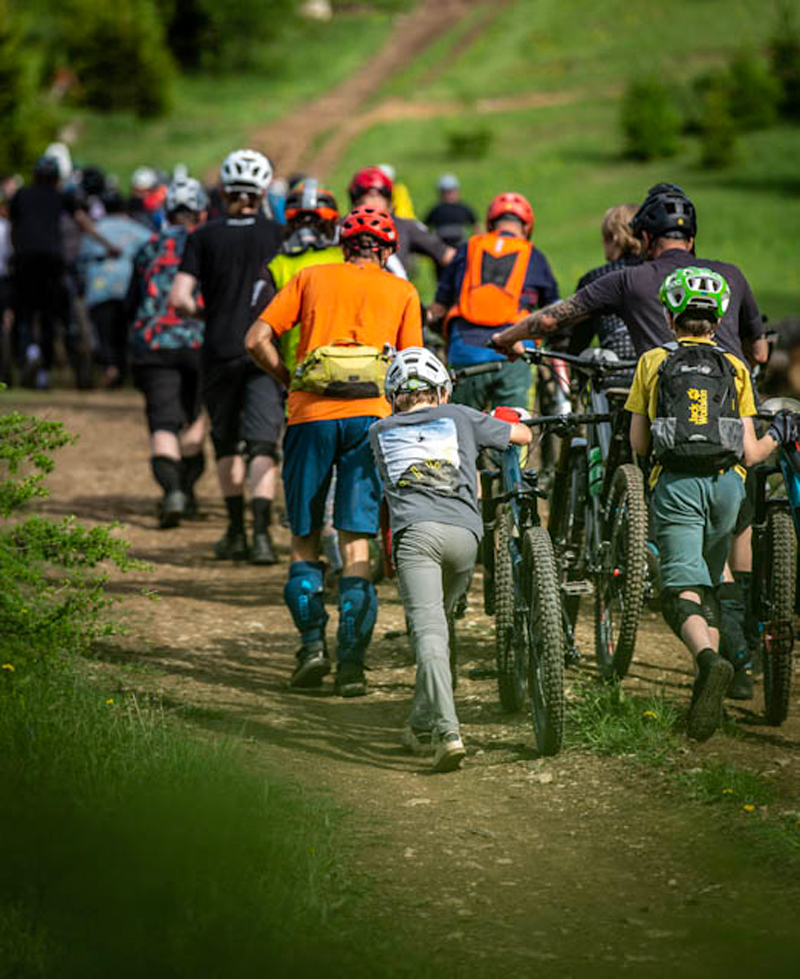 Die Teilnehmer und Teilnehmerinnen schieben ihre Bikes den Berg hinauf.