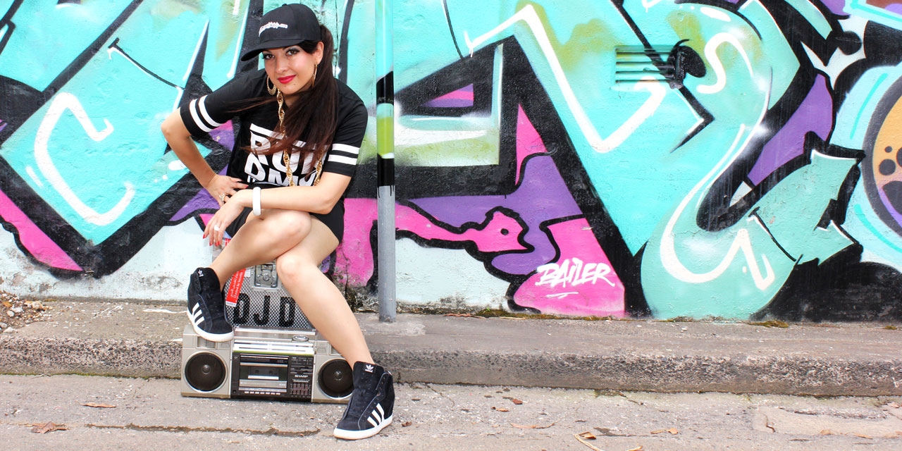 DJ D. sitzt auf einer Boombox vor einer Graffiti-Wall
