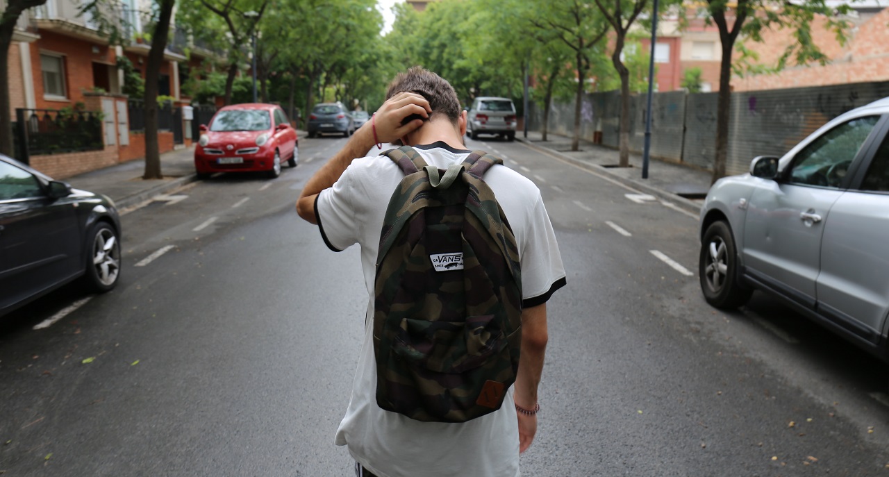 Junger Mann mit Rucksack von hinten, eine Straße entlanggehend