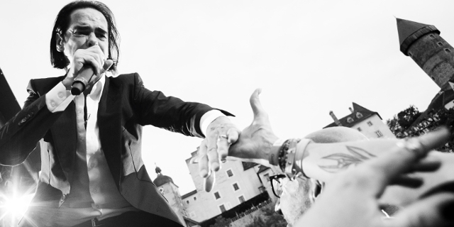 Nick Cave auf Burg Clam - er reicht einem Fan seine Hand, während er singt