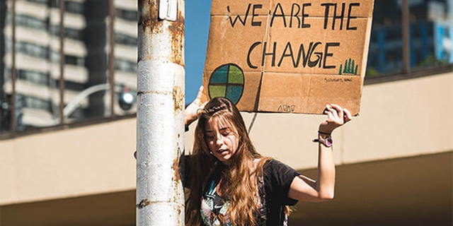 Eine junge Frau hält ein Schild hoch mit der Aufschrift "We are the change"