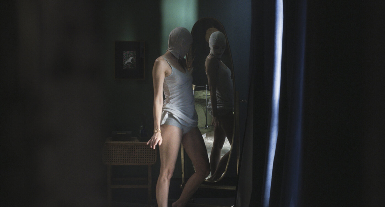 Eine Frau, deren Kopf einbandagiert ist, steht vor einem Spiegel
