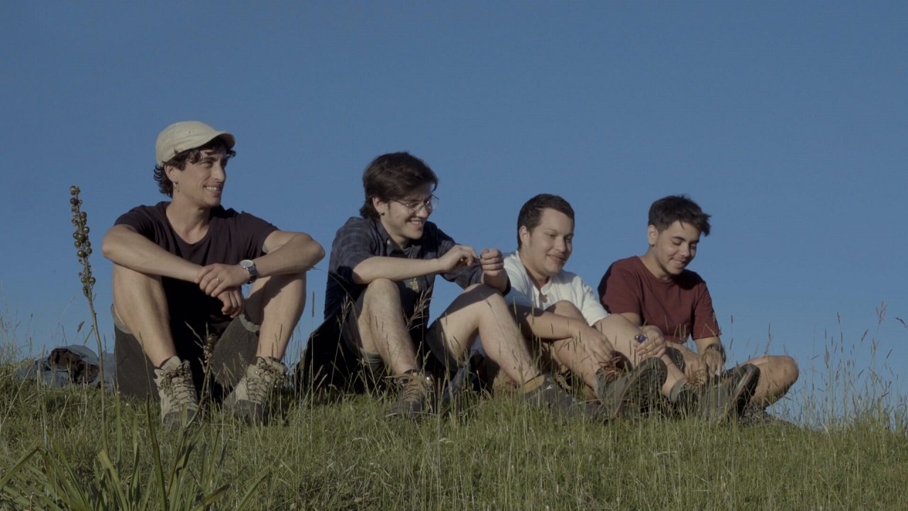 Vier junge, trans Menschen sitzen im Freien auf einem Hügel im Sommer. Szene aus der Doku "Into my name".