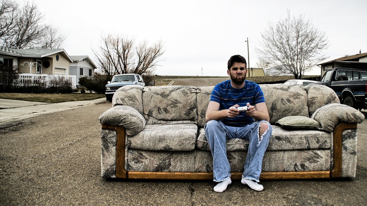 Ein Mann mit Bart sitzt auf einer Couch im Freien und hat einen Gamecontroller in der Hand.