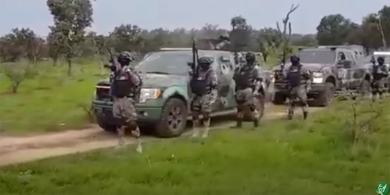 Mitglieder des Cártel de Jalisco in Militärmontur posieren mit schweren Waffen vor Panzern