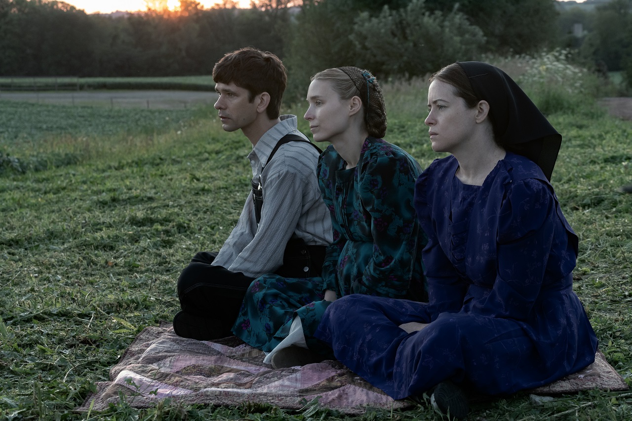 Drei Schauspielerinnen von "Die Aussprache" sitzen in maßgeschneiderten Kleidern auf einer Wiese.