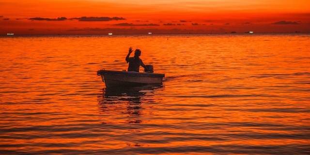 Mann in einem Boot im Sonnenuntergang winkt (Silouette)
