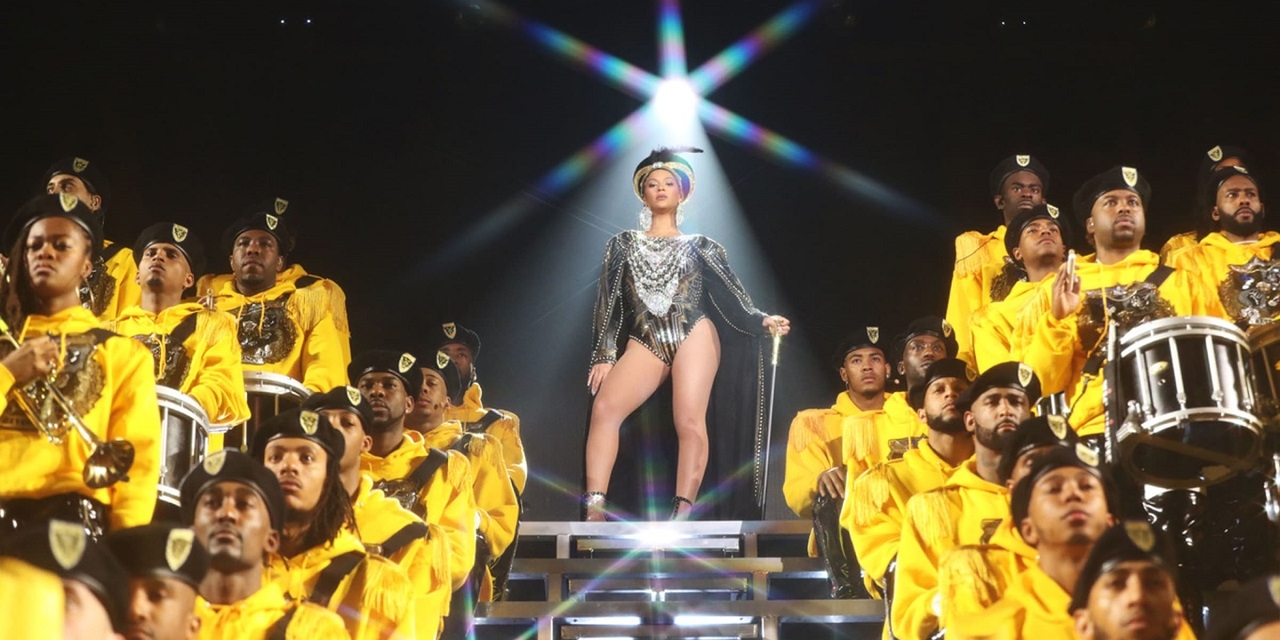 Beyoncé onstage in einem glitzernden Kostüm, umgeben von gelbgekleideten Männern