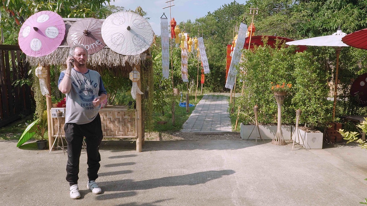 Ein Österreicher steht in Chiang Mai vor einem Garten. Szene aus "Good Life Deal".