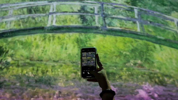 Eine Frau fotografiert einen Bildschirm, auf dem Werke des französischen Malers Claude Monet bei der “Monet am Wasser”.