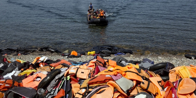 Boot mit geflüchteten Menschen am Weg zum Strand, dort Berge an Rettungswesten