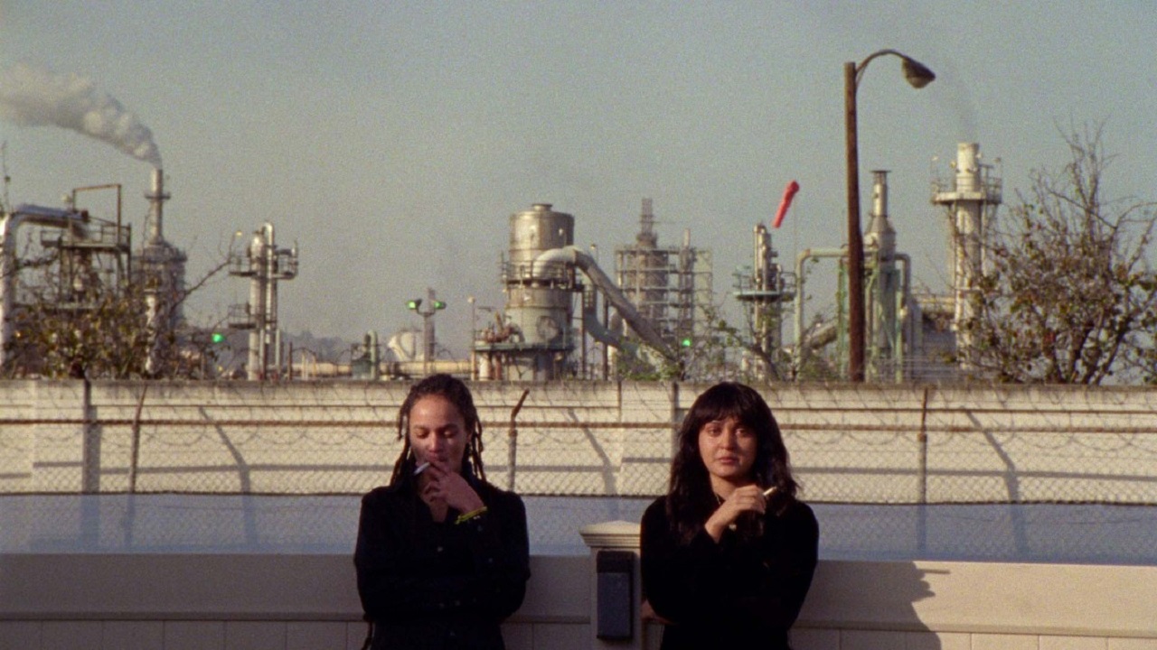 Zwei junge Frauen sitzen am Rande einer Ölraffinerie.