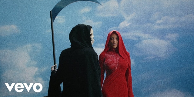 Doja Cat - „Paint The Town Red“ Screenshot aus dem Video, Doja Cat im roten Kleid steht neben einem Tod mit Sichel