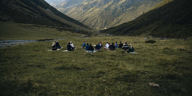 eine Menschengruppe macht Yoga auf der Wiese, im Hintergrund sieht man Berge