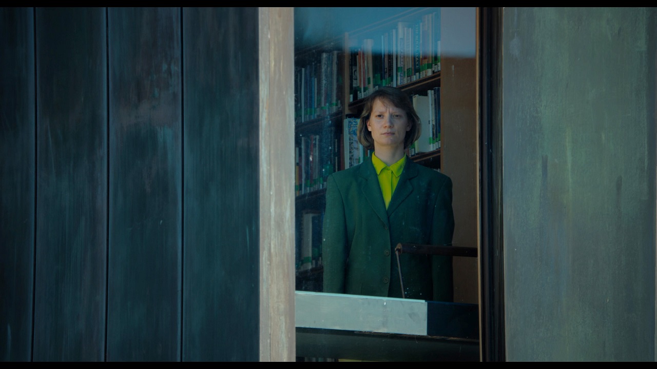 Mia Wasikowska steht hinter einem Fenster in einem Schulgebäude in "Club Zero".
